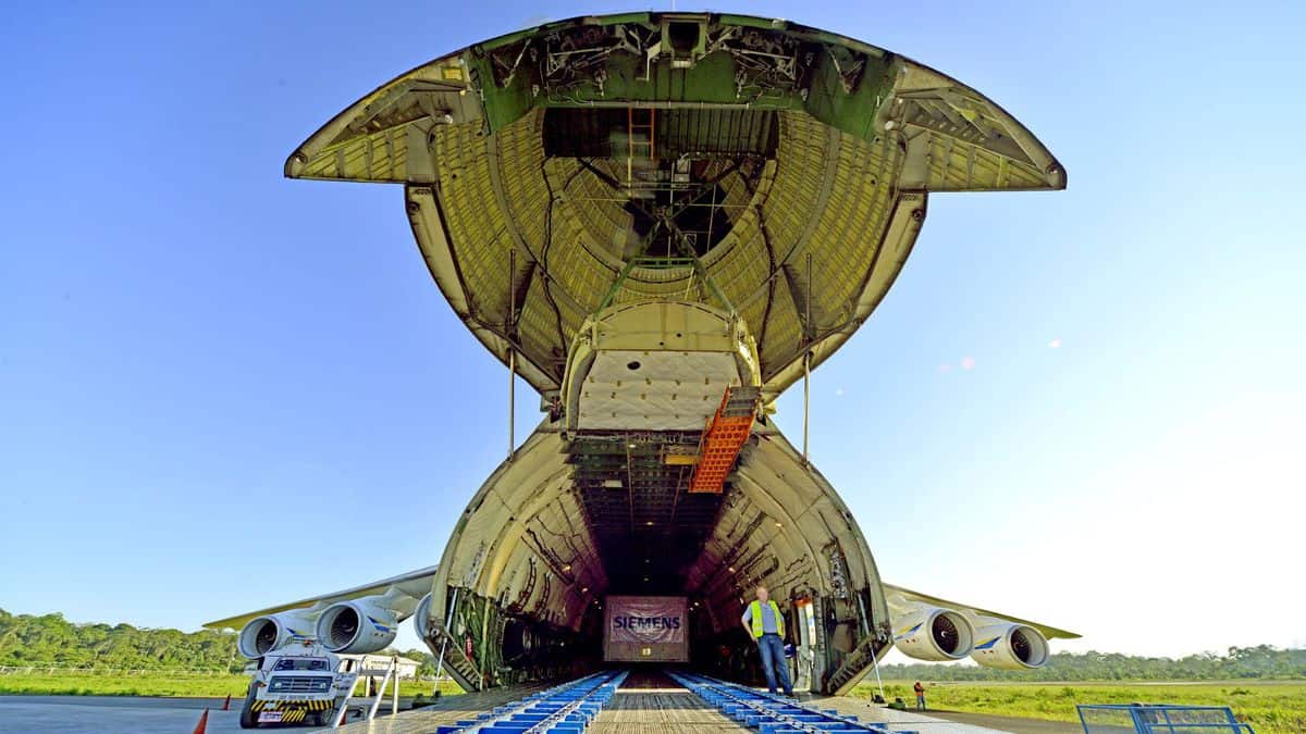 A massive cargo plane with its nose lifted open for loading on its ramp.