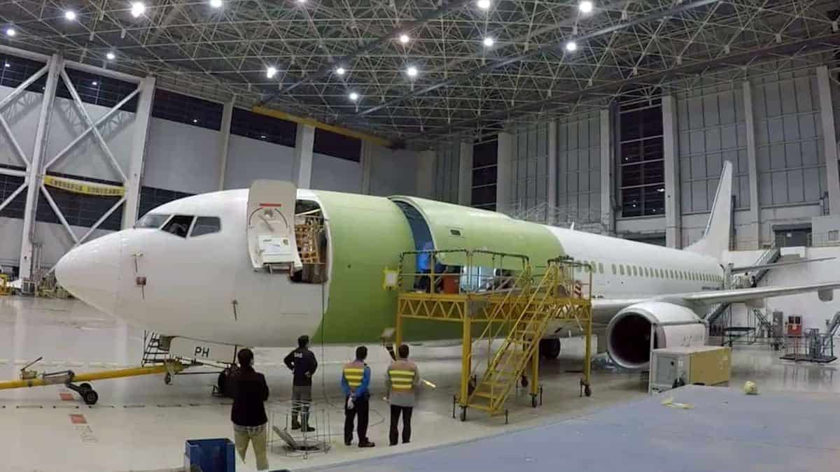 A Boeing 737 in a giant garage where it is being retrofitted with new equipment to carry cargo instead of passengers.