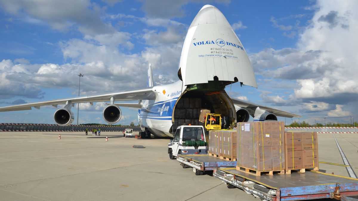 Huge cargo plane with its nose cone lifted so cargo dollies can be wheeled in.