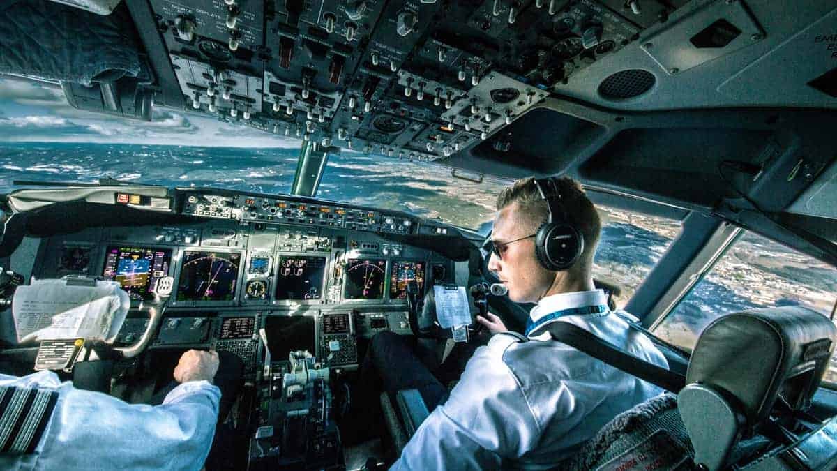 Pilots in cockpit looking out at sky, ground below..