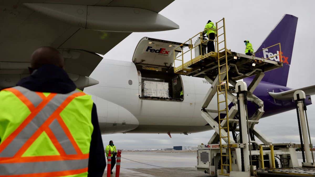 Hydraulic equipment lifts containers to rear door of a FedEx airplane.