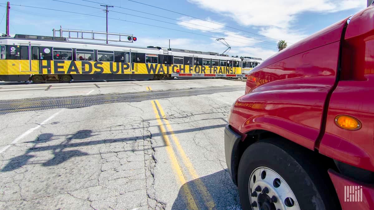 A photograph of a truck at a rail crossing waiting for a passenger train to go by.