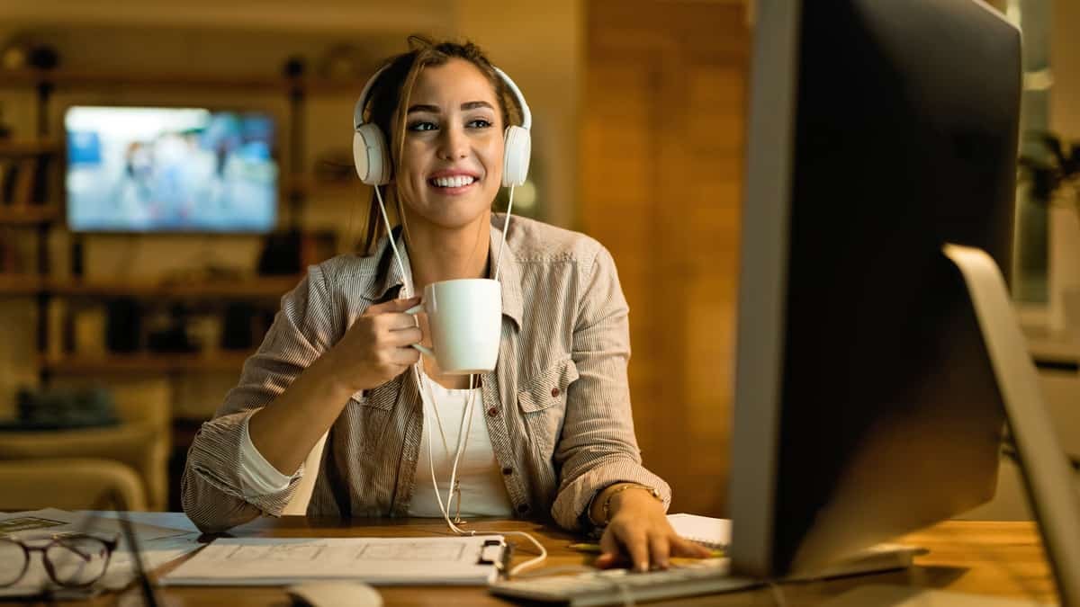 Woman with headphones and white mug sitting at a desk working