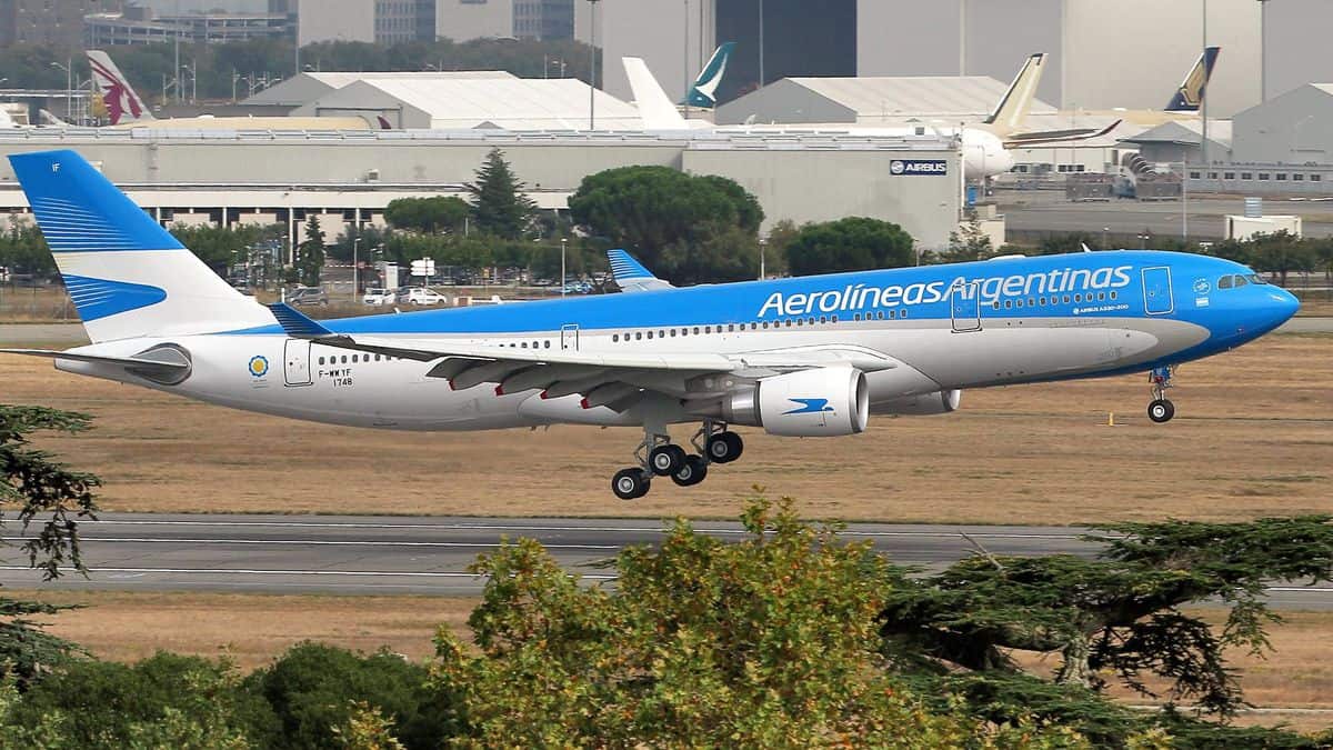 A blue-and-white jet comes in for landing with wheels down.