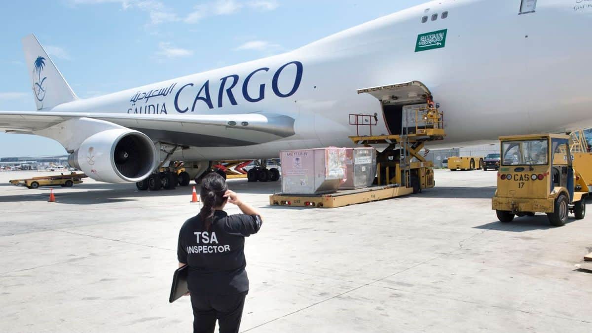 A TSA inspector watches a Saudia plane being loaded with pallets of cargo.