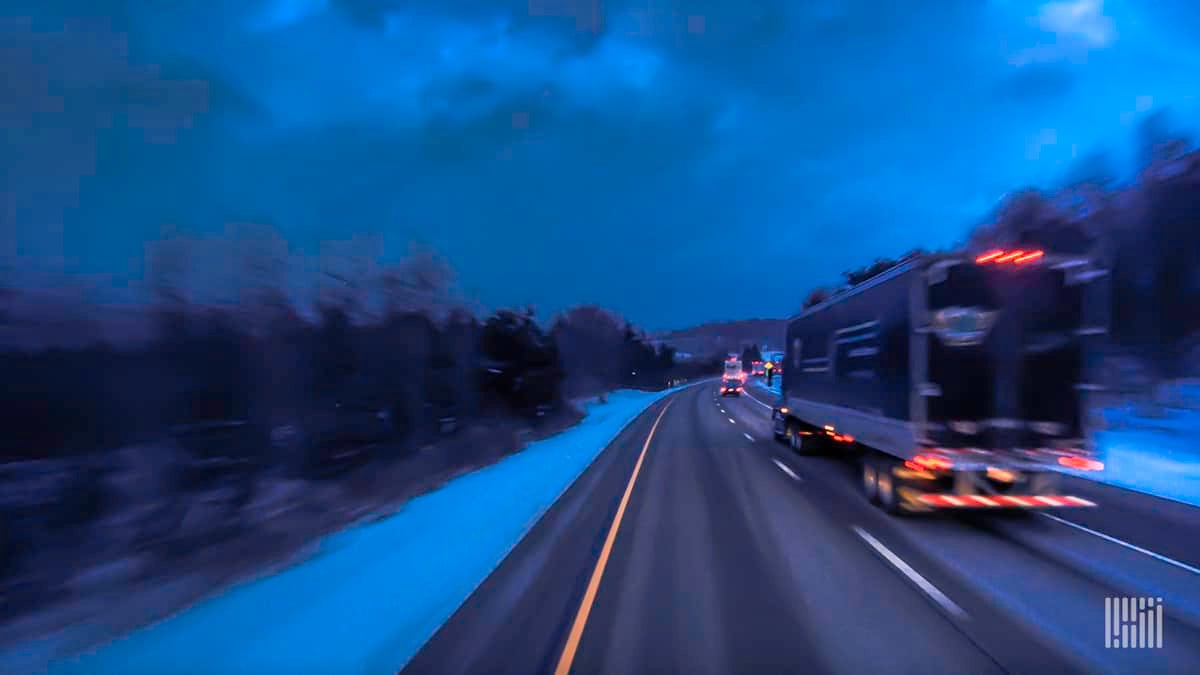 Tractor-trailer heading down slushy road at night.