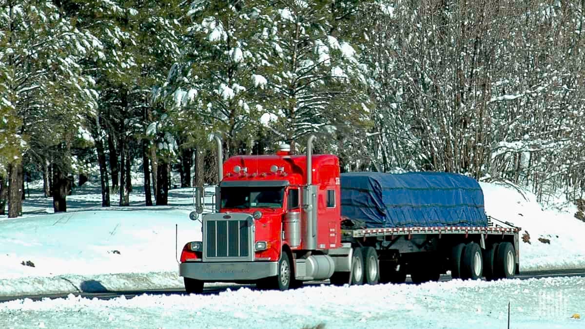 Flatbed tractor-trailer heading down a snowy road.