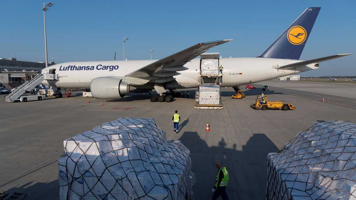 A white Lufthansa plane with blue tail and cargo pallet sitting on ground.