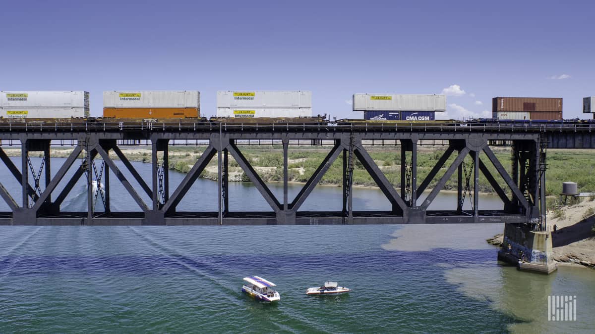 A photograph of a train crossing over a bridge. The train is hauling intermodal containers.