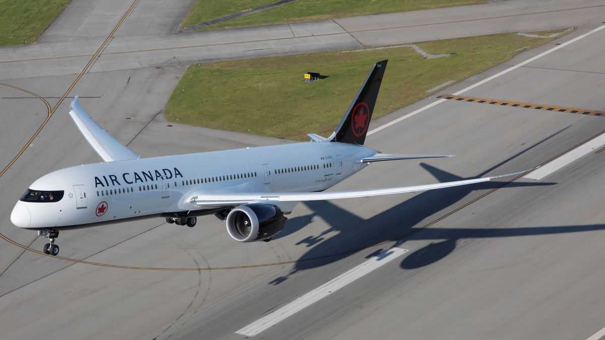 A white jet lifts off the runway. View from above and in front of plane.