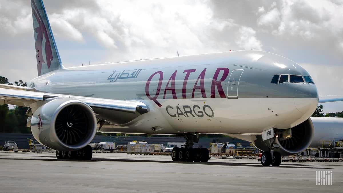 A Qatar Airways Cargo jet, beige on top and white on bottom parked on a sunny day.