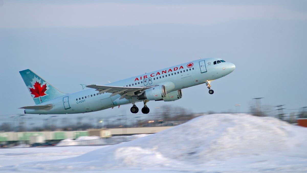 A gray/white Air Canada jet takes off on an overcast day with snow in the foreground.