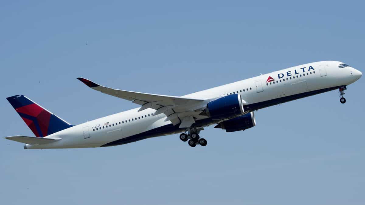 A white Delta jet with blue tail against a blue sky looking up as it passes over on takeoff.