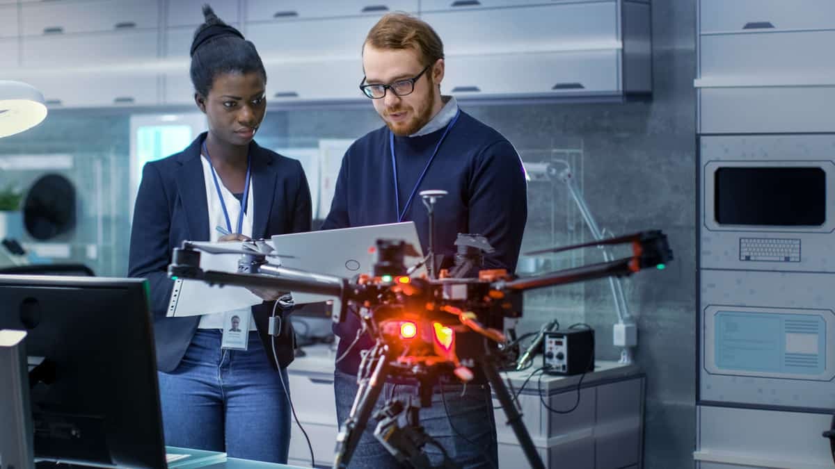 Two people look at a document with a drone positioned in the foreground.