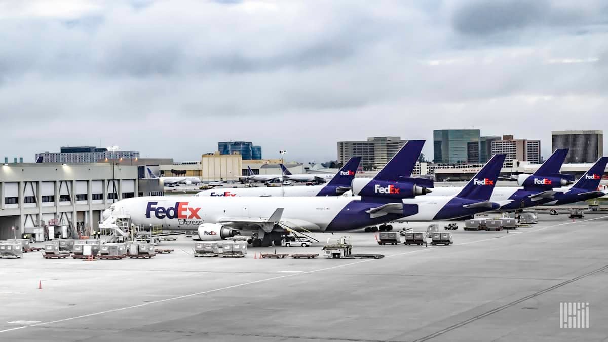 FedEx aircraft, white with blue tails, parked at airport.