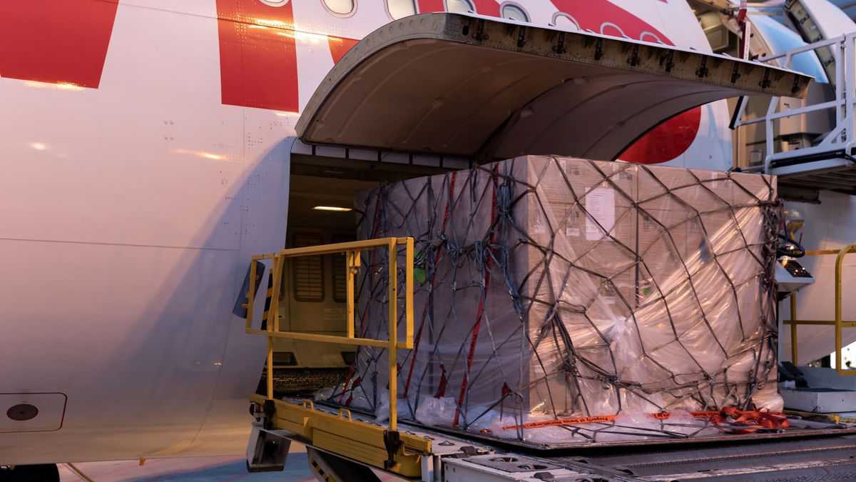 A large pallet of cargo on a hydraulic lift gets loaded into the side door of a plane.