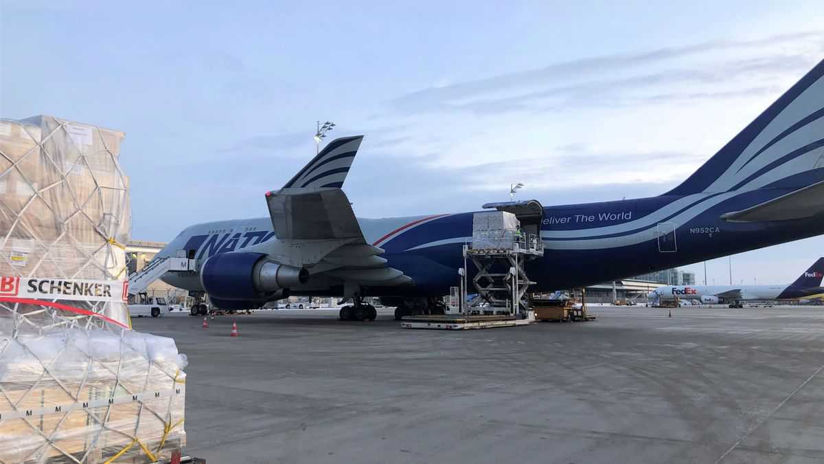 A cargo pallet sitting on tarmac next to a big white and blue jumbo jet.