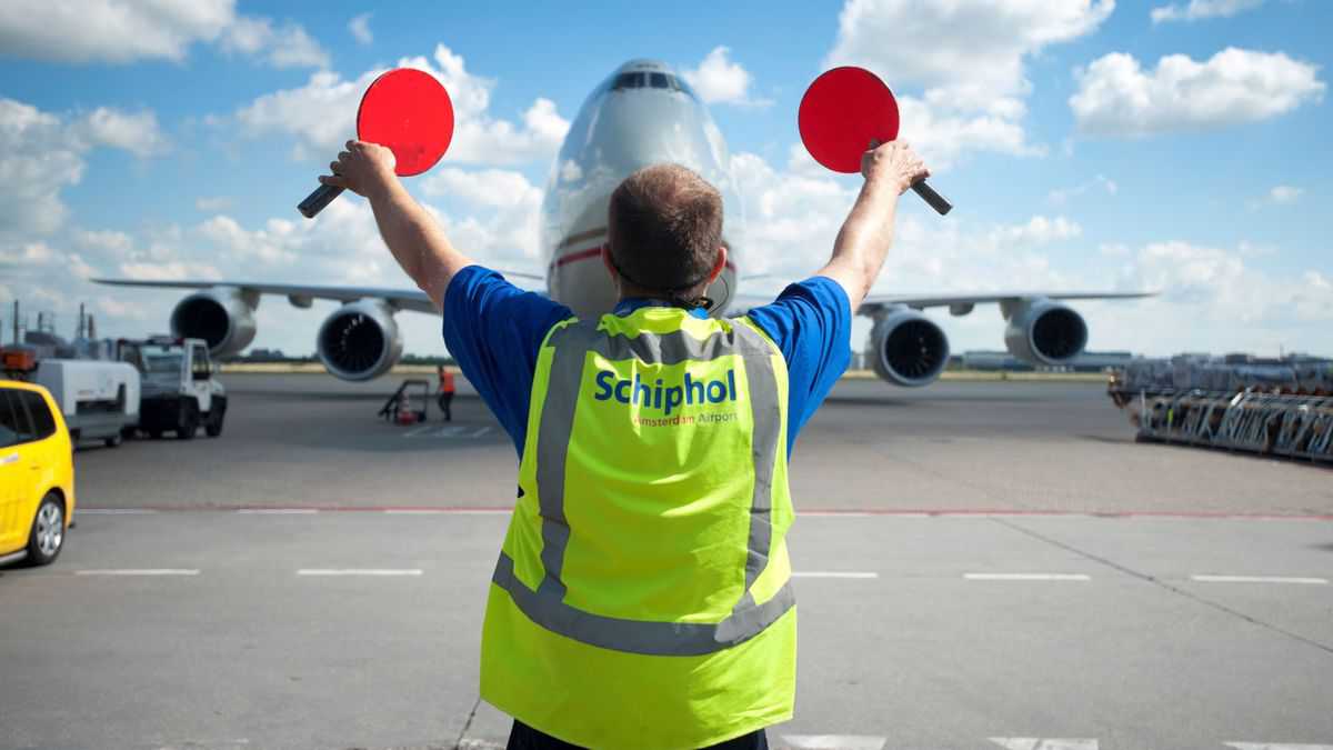 Ground crew person with yellow vest and paddles to wave plane to parking spor.