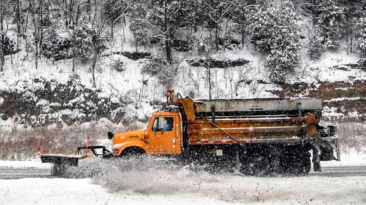 Plow truck clearing snow covered mountain highway.