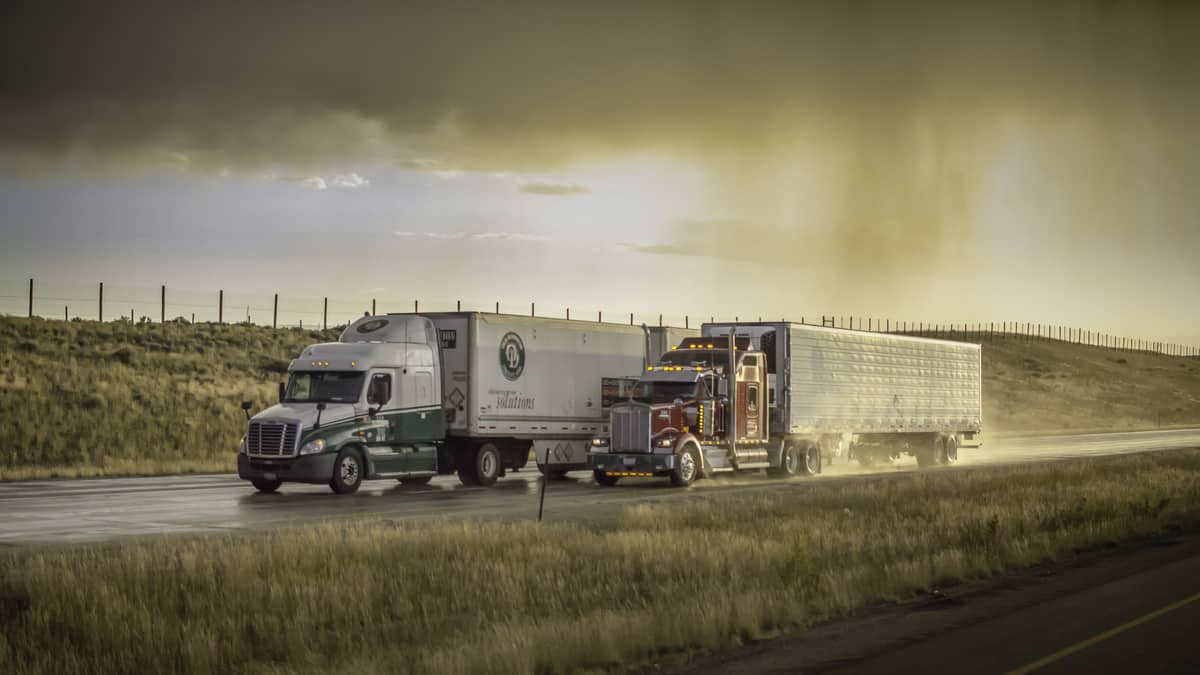 Tractor-trailers heading down highway with storm cloud on the horizon.