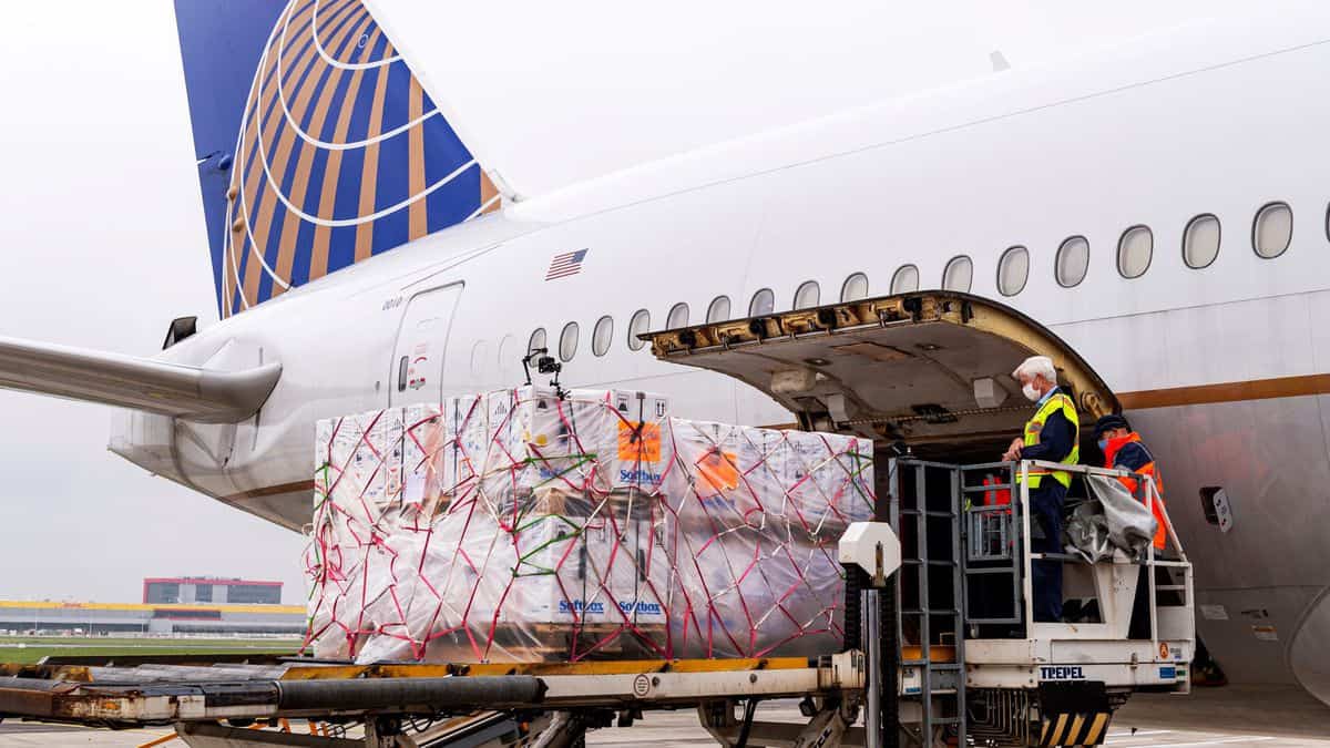 Plastic wrapped pallets of cargo loaded in side door of white United jet, with blue tail.