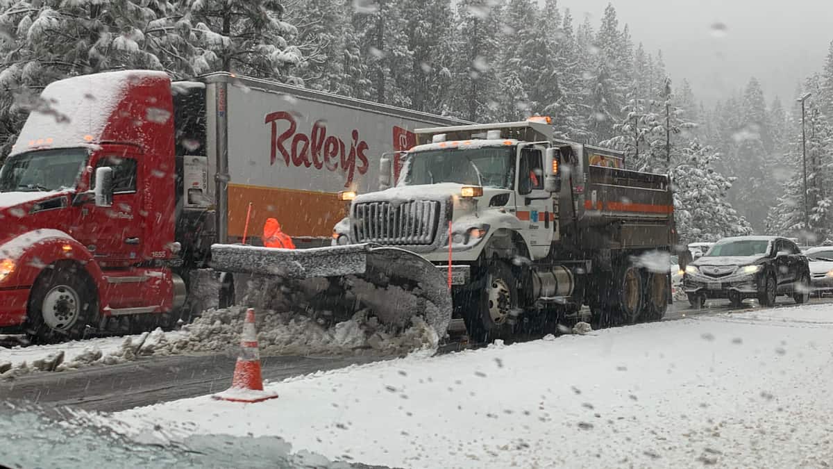 Tractor-trailer, other vehicles stopped on snowy Sierra Nevada highway.