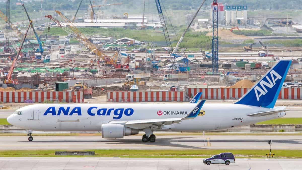 A white All Nippon Airways cargo plane with blue tail moves down a taxiway at Bangkok airport, with construction in the background.