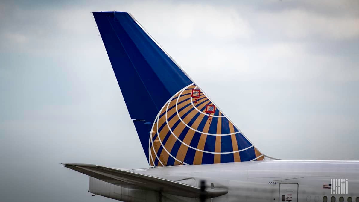 Blue tail fin of a United jet against a gray sky.