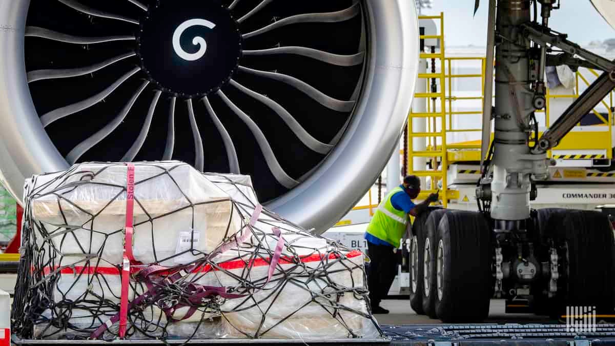 A cargo pallet rests on the ground in front of a big jet engine.