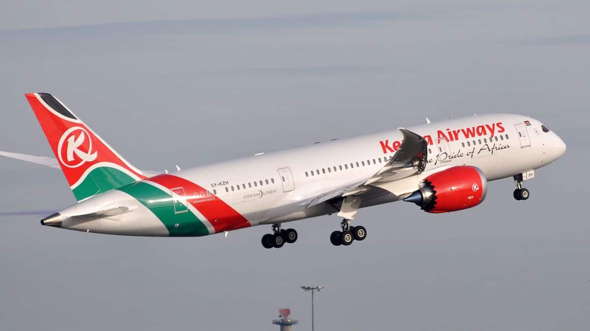 A white jet with red tail on take off with wheels still down. Kenya Airways.