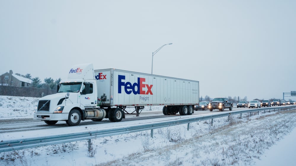 FedEx truck heading down snowy Pennsylvania highway with traffic behind it.