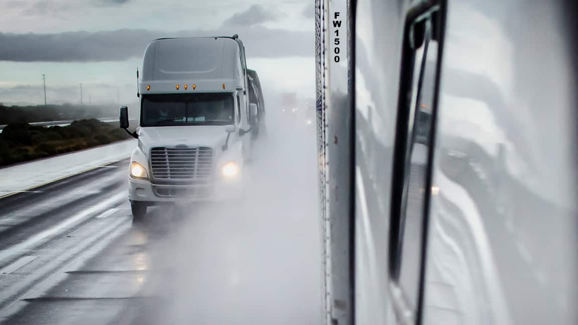 Tractor-trailers heading down a wet highway.