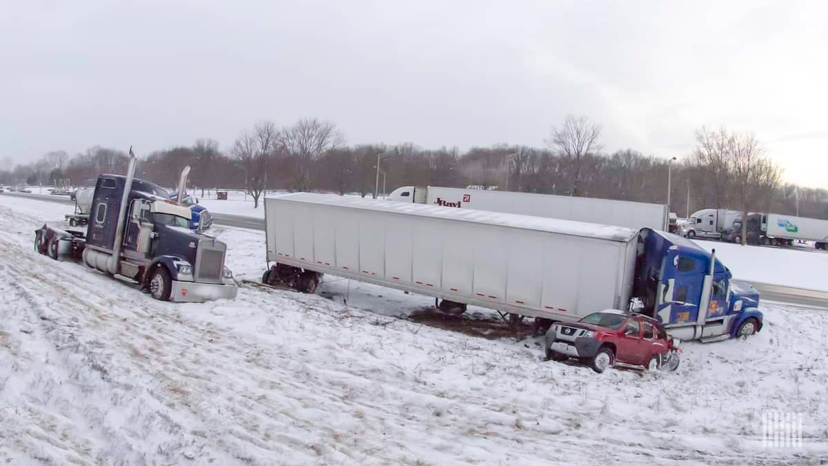 Tractor-trailers and cars stuck on side of snowy highway.