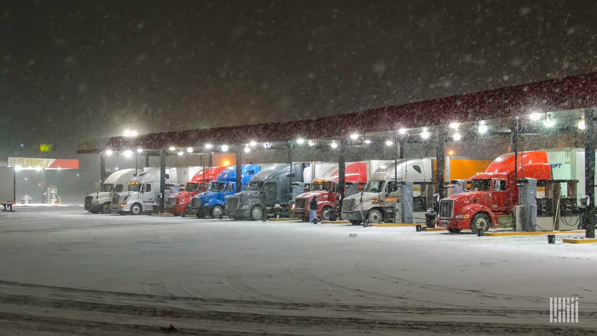 Tractor-trailers parked at a truck stop on a snowy day.