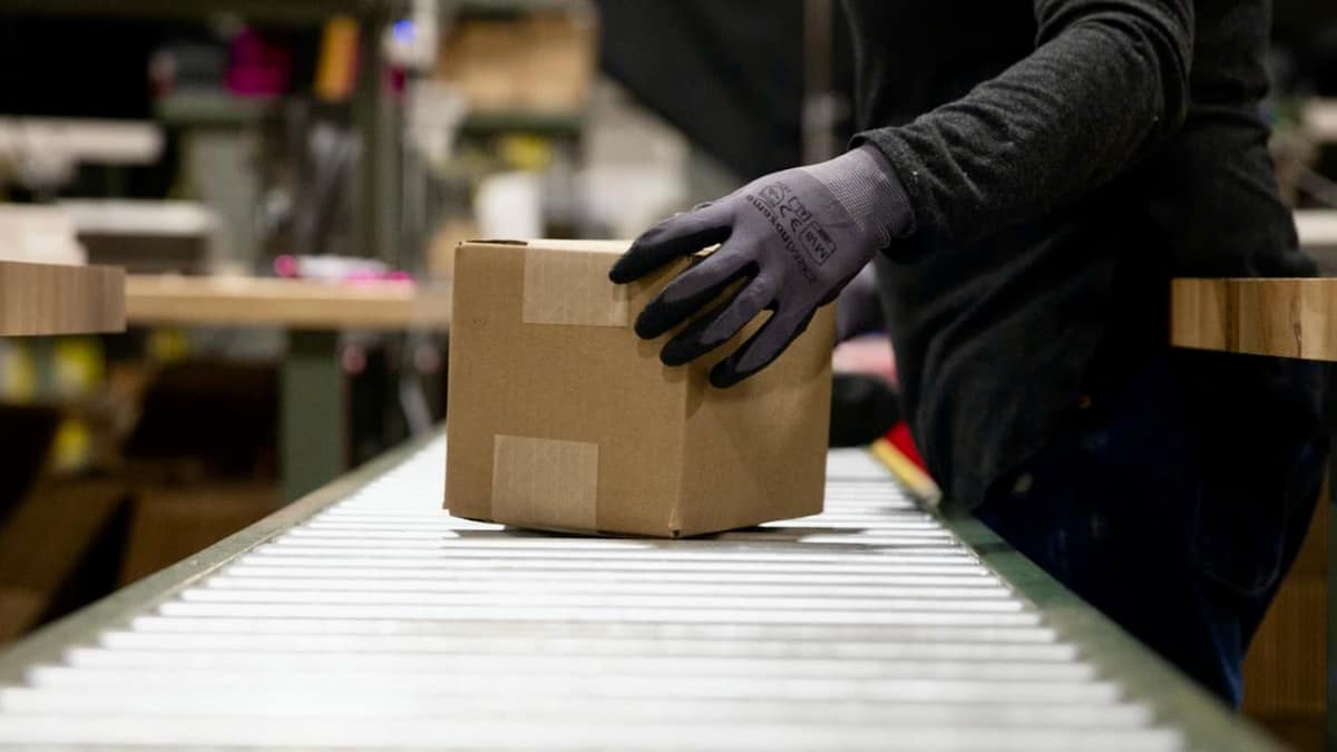 A package is handled by a warehouse worker wearing gloves at a Shopify fulfillment network facility.