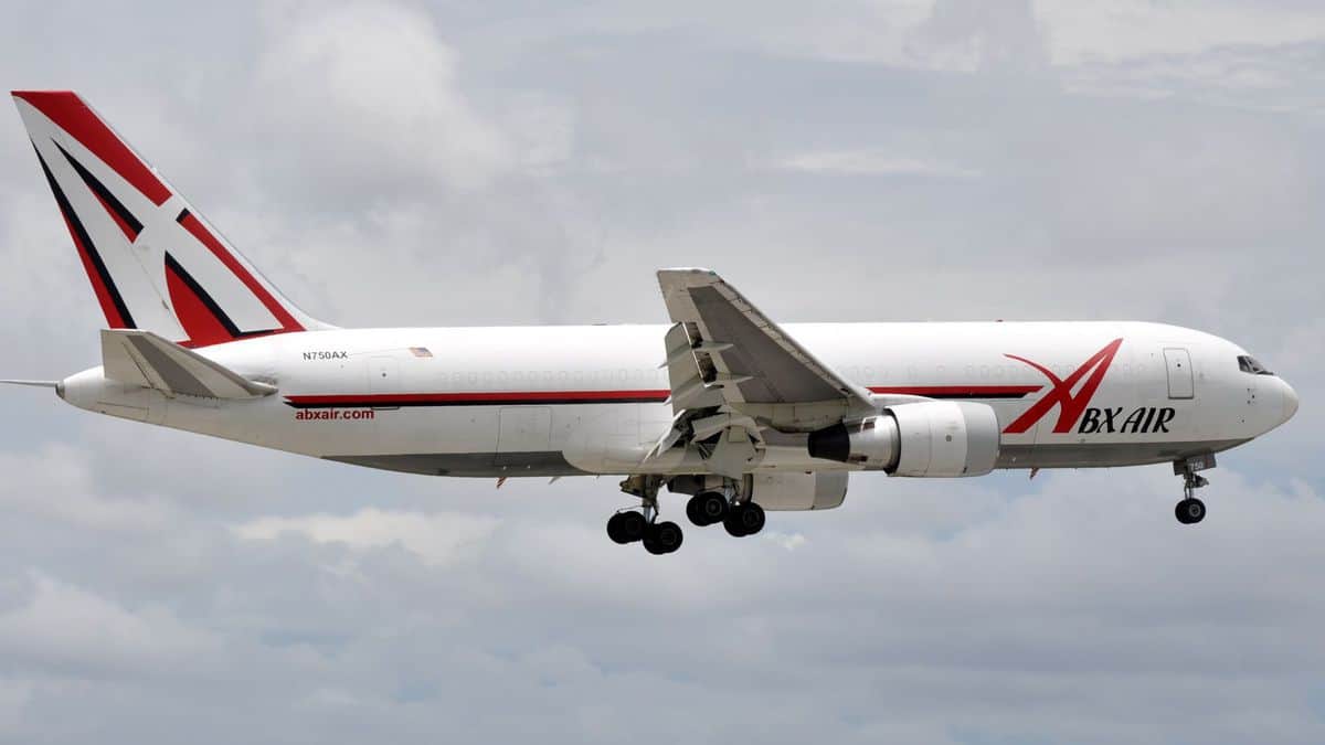 A large white plane with wheels down comes in for a landing.