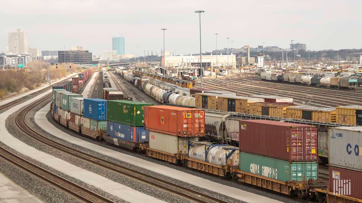 A photograph of a rail yard with parked railcars and intermodal containers.