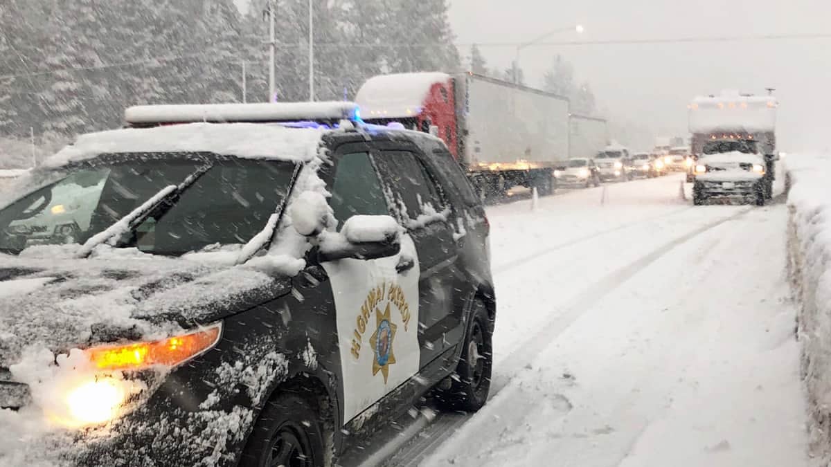 Cars and semis stopped by the CHP on a snowy California highway.