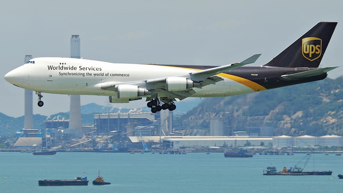 A white UPS jumbo jet with brown tail coming in for landing over water by Hong Kong Airport.