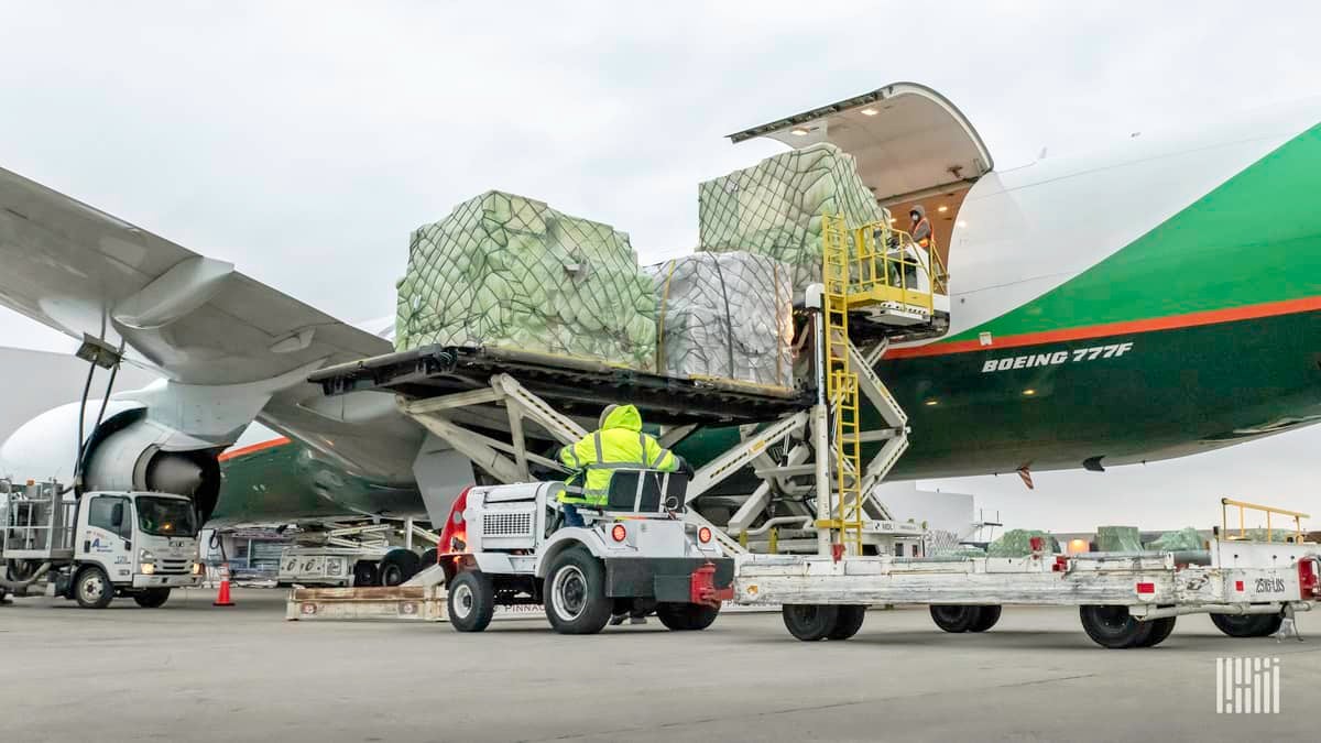 A white and green plane loading pallets of cargo through side door.