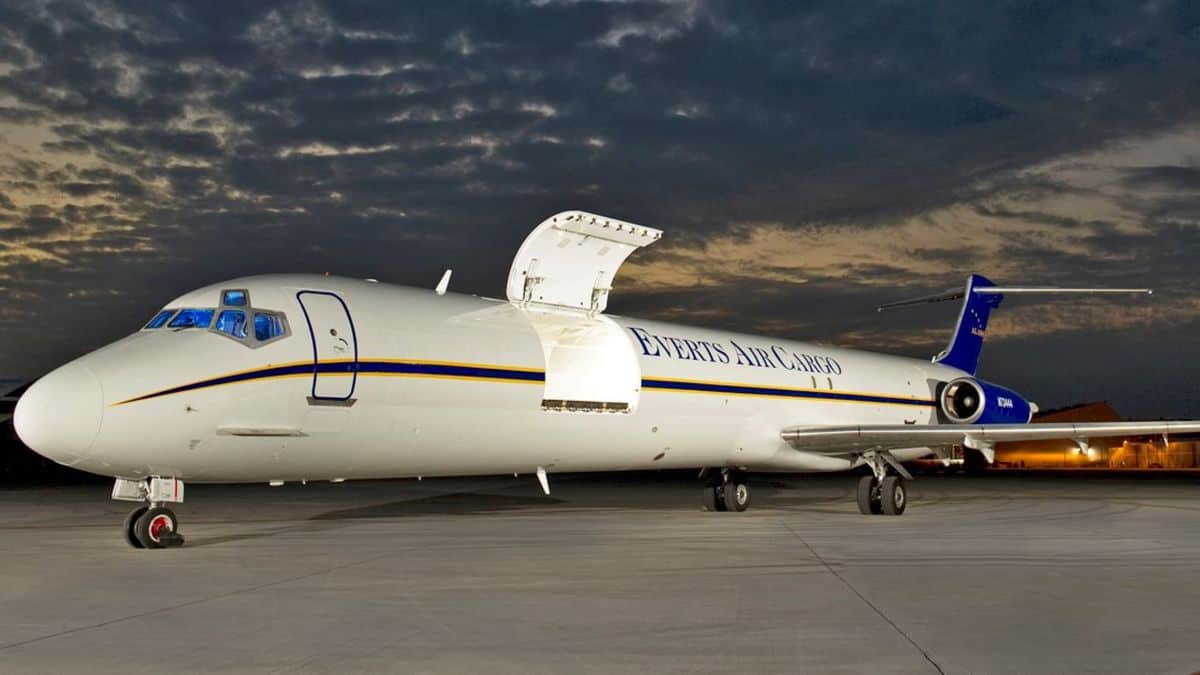 A white MD-88 aircraft with side cargo door open at night.