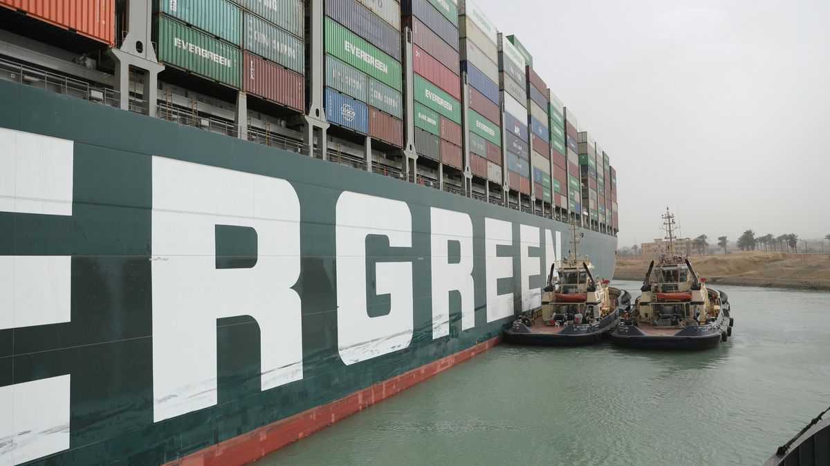 Tug boats try to move a big green container ship stuck in the mud.