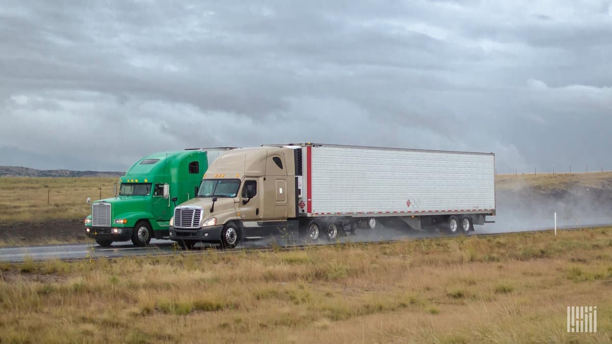 Two tractor-trailers heading down a wet highway.