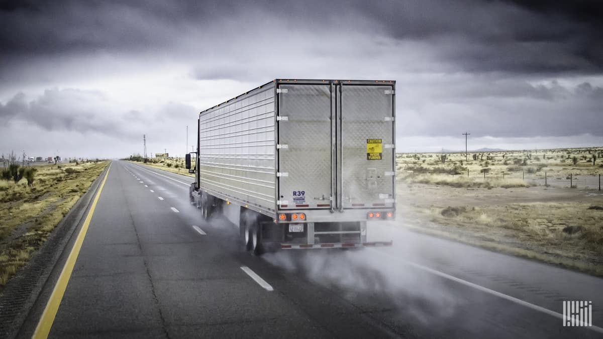 Tractor-trailer heading down wet highway.