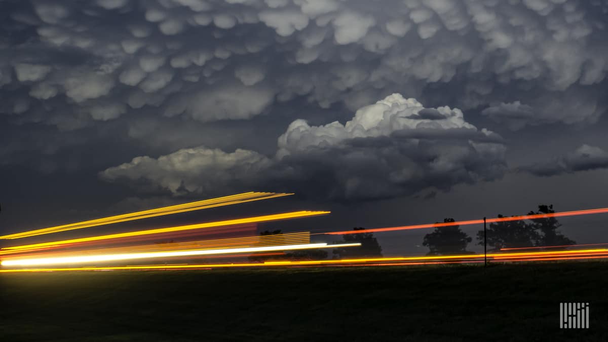 Cars and trucks on a highway, with storm cloud across the sky.