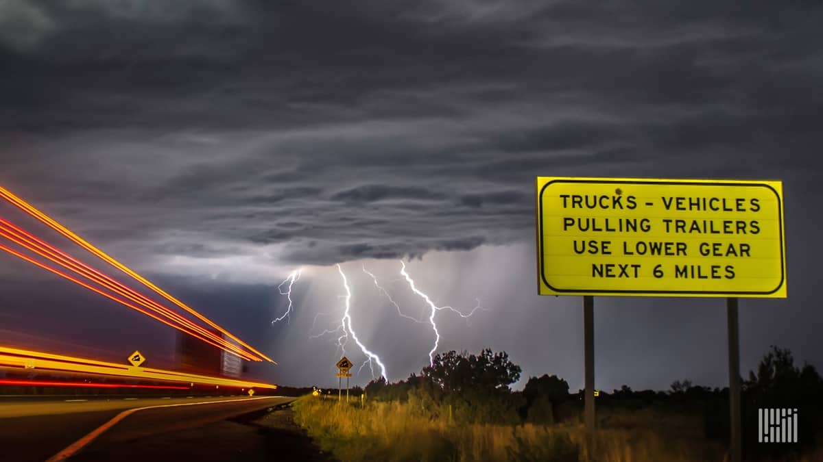 Car and trucks on a highway with lightning bolt coming down from a storm ahead.