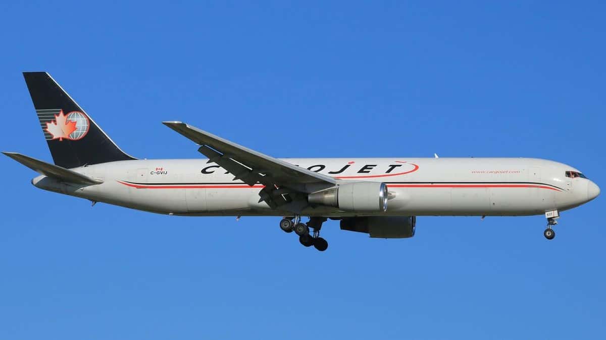 A white Cargojet plane with blue tail in blue sky comes in for landing, with side view from below