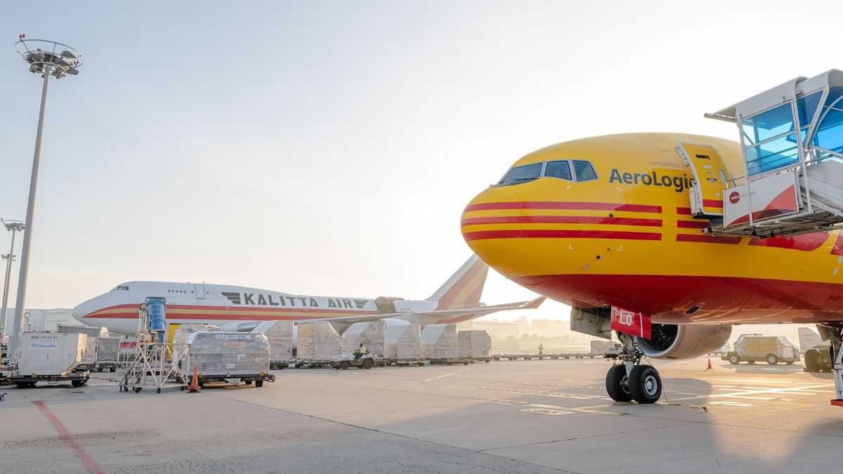 A bright mustard-yellow plane in the foreground, nose shot only, and a white cargo jet in the background at an airport.