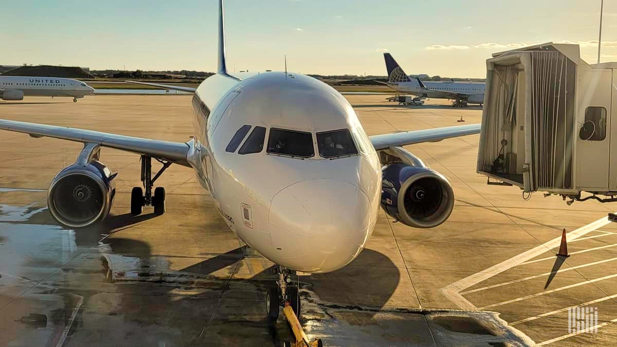 A small passenger jet parked at the gate on a sunny morning, looking straight out at cockpit.