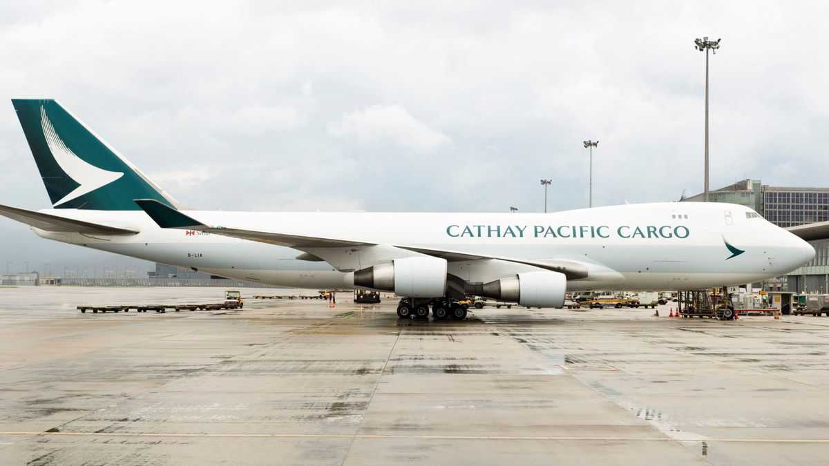 A white 747 jumbo jet with a green tail operated by Cathay Pacific Cargo sits on a wet tarmac.